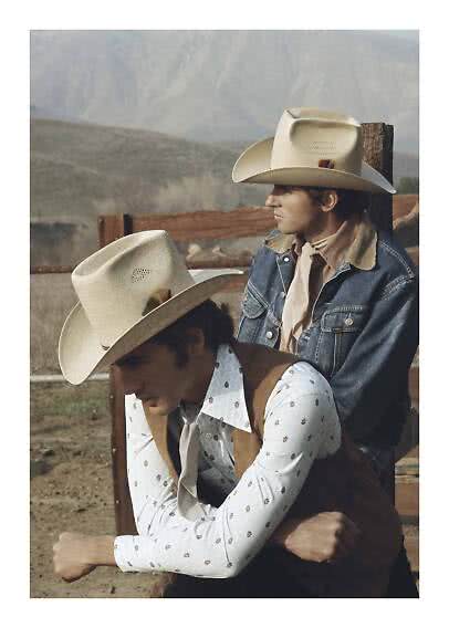 Due uomini con cappelli da cowboy e abiti western accanto a una staccionata in paesaggio arido