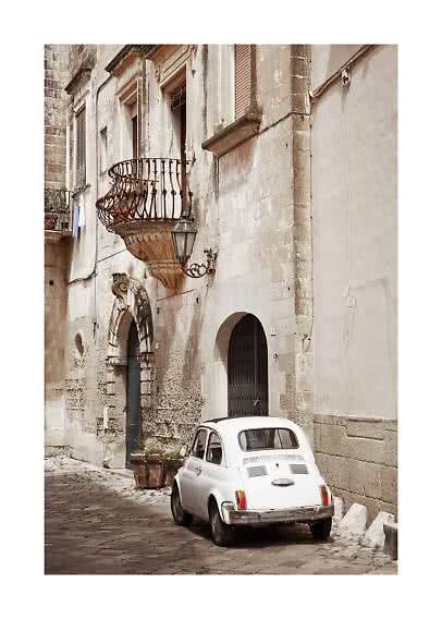 White vintage car parked on a narrow cobblestone street beside an old stone building with balcony
