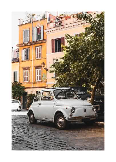 White vintage car parked on a cobblestone street beside warm-toned buildings and trees