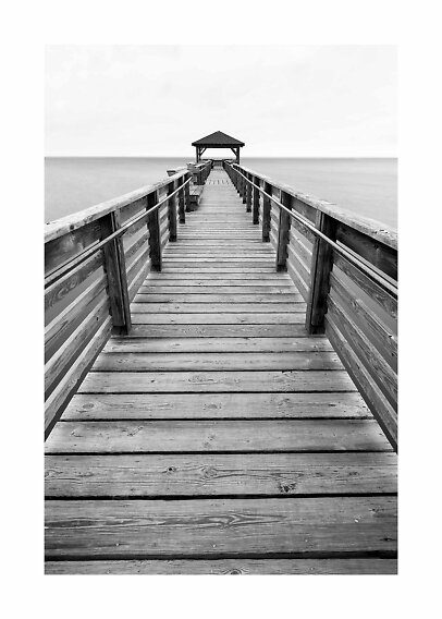 Black and white photo of a long wooden pier with railings leading to a small gazebo over the water