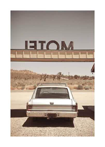 Vista traseira de um carro clássico prateado sob uma placa de motel no deserto