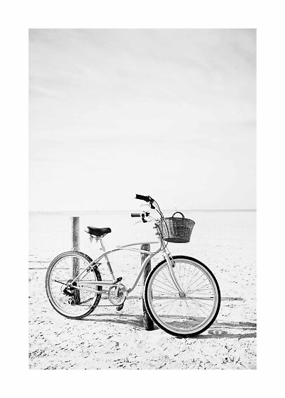 Hvid citybike med flettet kurv parkeret på en sandstrand i sort-hvid