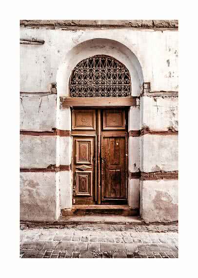 Old wooden door in an arched doorway with wrought iron grille on a weathered white wall
