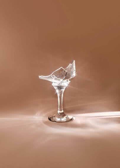 Krossat cocktailglas på fot mot beige bakgrund med glittrande ljusreflexer