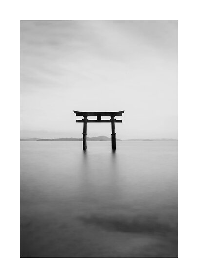 Black-and-white photo of a Japanese torii gate in calm water with mountains in the distance