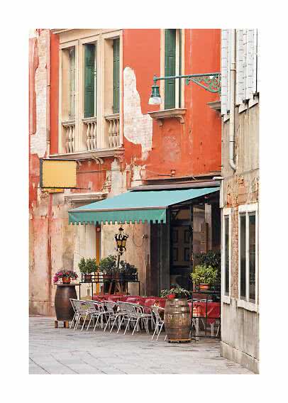 Café al aire libre con mesas y sillas junto a un edificio naranja con contraventanas verdes