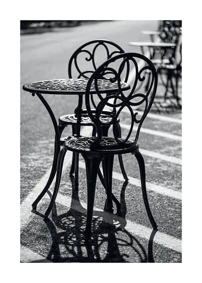 Black café table with two ornate metal chairs on a wet street