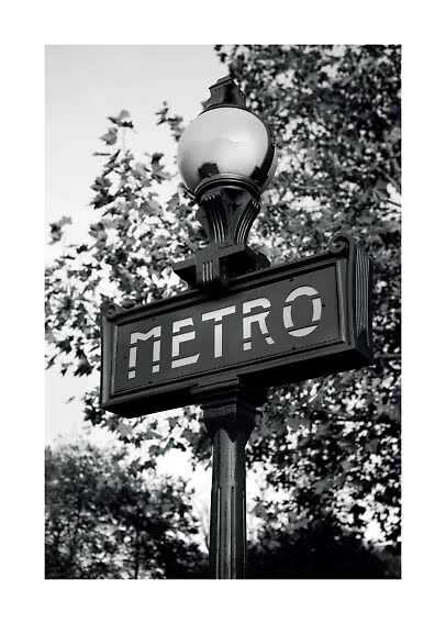 Insegna Metro in bianco e nero su un palo con lampada e alberi sullo sfondo