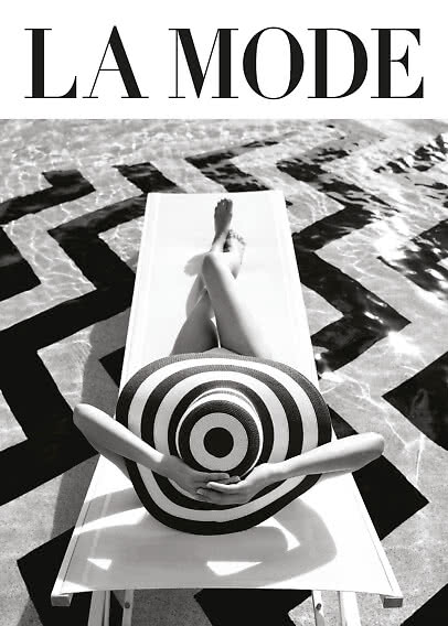 Black-and-white fashion image of person on lounger by pool with large striped hat