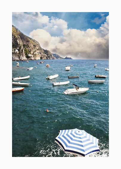 Coastal scene with small boats on the sea, cliffs on the left, and a blue sky with large clouds