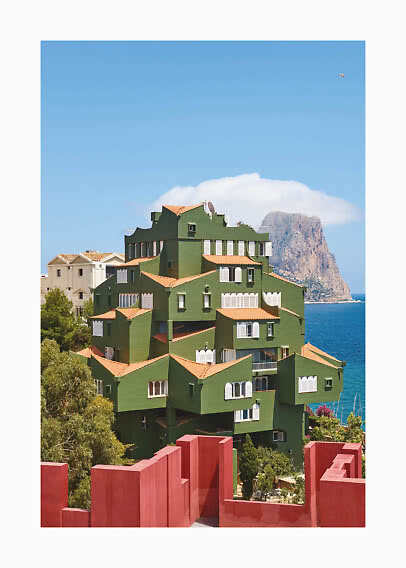 Green building with terracotta roofs by the sea, with rocky cliff and blue sky behind