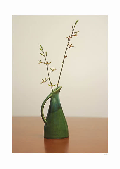 Grüne Keramikvase mit Henkel und zarten Blütenzweigen auf einem Holztisch