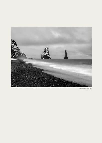 Foto in bianco e nero di una spiaggia di sabbia nera con faraglioni e onde sotto cielo nuvoloso