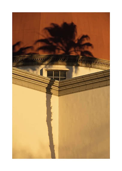 Schatten einer Palme auf heller Gebäudeecke mit kleinem Fenster und orangefarbener Wand