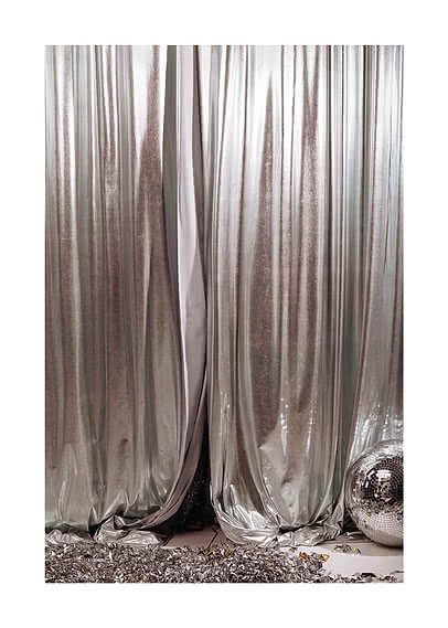 Photograph of silver lamé curtains in heavy vertical folds, a mirror ball resting against the fabric and foil confetti across the floor