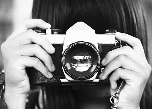 Primo piano in bianco e nero di mani che tengono una fotocamera vintage davanti al viso