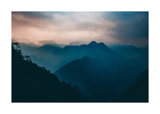 Siluetas de montañas brumosas al atardecer bajo un cielo dramático