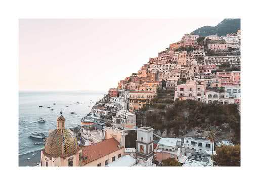 Pastel-colored coastal town on a steep hillside with church dome and boats on the sea
