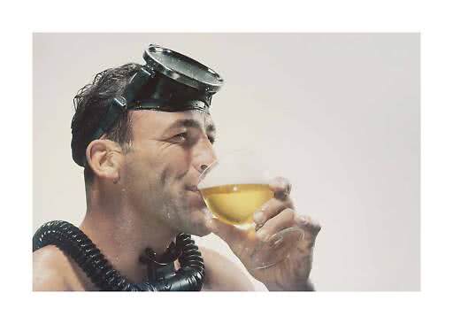 Man wearing snorkel gear drinks from a wine glass with a golden beverage