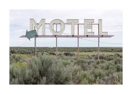 Großes altes Motel-Schild mit Pfeil in offener Buschlandschaft unter bewölktem Himmel