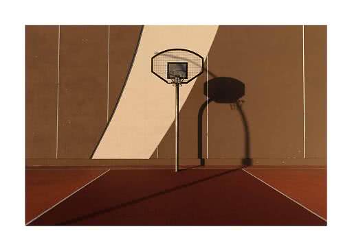 Basketballkorb auf einem Außenplatz vor brauner Wand mit langem Schatten im Sonnenlicht