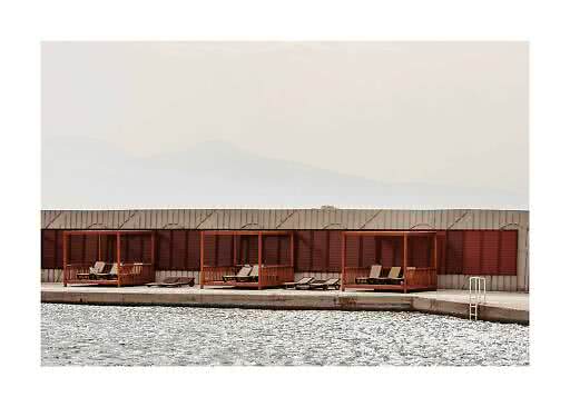 Cabañas de madera con tumbonas junto a una piscina, frente a una pared con persianas y montañas