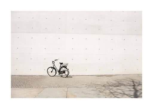 Bicicletta da città nera con cestino parcheggiata davanti a un grande muro di cemento chiaro
