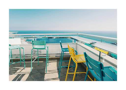 Rooftop terrace with colorful bar stools and glass railing overlooking the sea