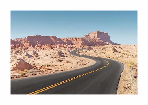 Carretera asfaltada sinuosa por el desierto con rocas rojas bajo un cielo azul despejado