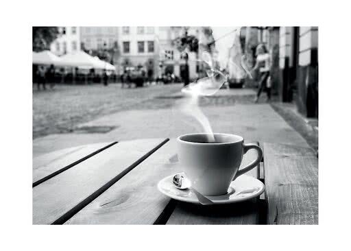 Steaming coffee cup on saucer with spoon on a wooden table at an outdoor café, black and white