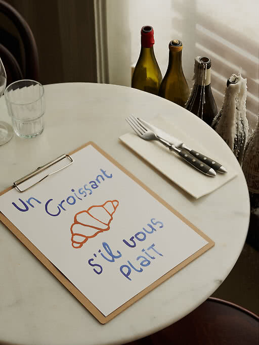 Affiche Un Croissant sur une table en marbre à côté de couverts et de bouteilles de vin