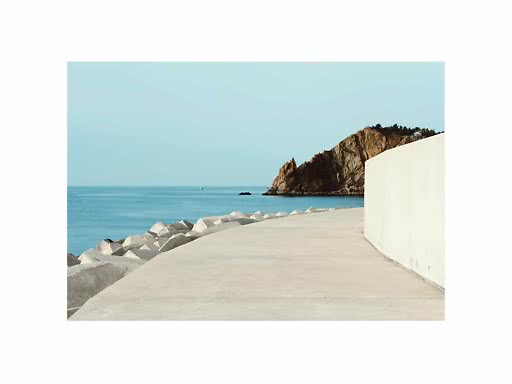 Curved concrete seaside walkway with rocks and calm blue water