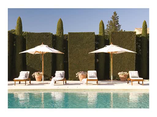 Bordo piscina con quattro lettini, due ombrelloni bianchi e alte siepi potate