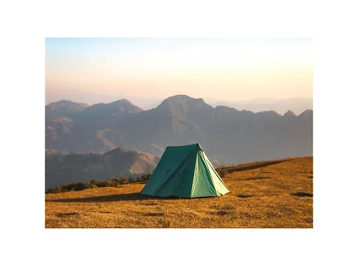 Grünes Zelt auf goldenem Hügel mit Berglandschaft im Hintergrund bei Sonnenuntergang