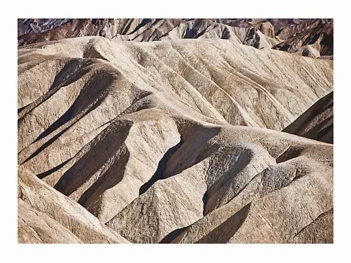 Colline desertiche beige ondulate con ombre profonde e formazioni rocciose stratificate
