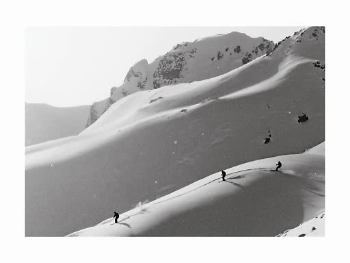 Trois skieurs sur une pente enneigée en montagne, en noir et blanc