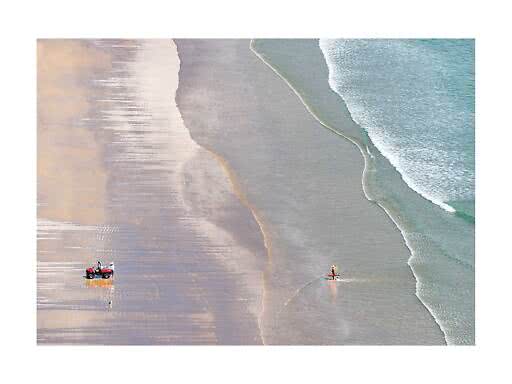 Aerial view of beach with waves, wet sand, an ATV and a person carrying a surfboard