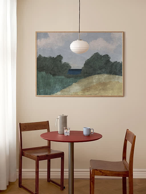 Spisehjørne med rødt rundt bord, to træstole, lampe og stort landskabsmaleri på beige væg