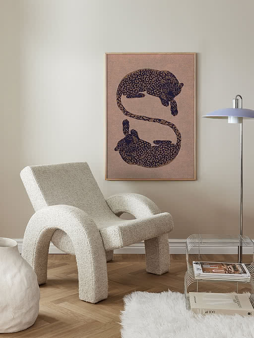 Plakaten Elegant Leopards i egeramme på knækhvid væg over en hvid bouclé-lænestol, med keramikvase, fåreskindstæppe og kromet bladholder