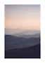 Siluetas de montañas en capas en suaves tonos morados bajo un cielo claro al amanecer