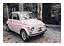 Light pink vintage car parked on a cobblestone courtyard in front of a leafy building