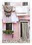 Laundry hanging on a line outside a pink house with striped door curtain and flower box
