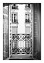 Schwarz-weißer Blick durch offenes Fenster mit schmiedeeisernem Balkon auf Haus mit Balkonen