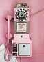 Rosa Retro-Münztelefon mit Wählscheibe und Hörer an einer rosa Wand