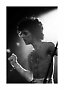 Foto de concierto en blanco y negro de un cantante sin camisa de perfil bajo un foco