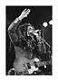 Foto en blanco y negro de cantante con rastas y guitarra en el escenario, cantando al micrófono