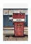 Vintage red gas pump labeled Unleaded in front of a blue and white building