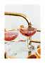 Two coupe glasses with pink cocktails and orange peel on a mirrored tray with gold handle