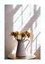 White ceramic pitcher with dried flowers on a round table in sunlight