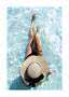 Person in black swimwear and a large straw hat sitting in clear shallow pool water, top view